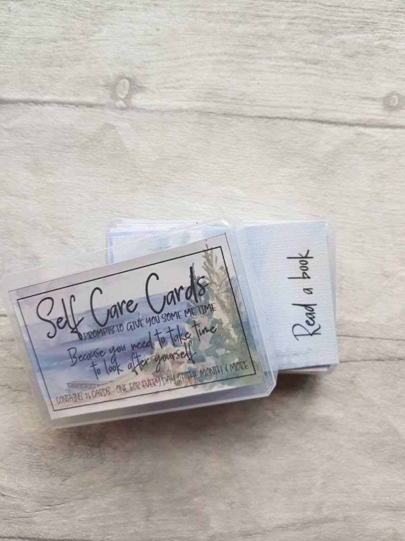 May include: A set of self-care cards in a clear plastic box with a watercolour design. The box has the text "Self Care Cards" and "Prompts to give you some me time because you need to take time to look after yourself". The box also says "Contains 36 cards - one for every day of the month & more".