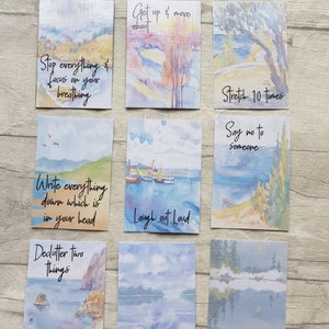 May include: Nine watercolour cards with inspirational quotes and painted landscapes. The quotes include "Stop everything & focus on your breathing", "Get up & move about", "Write everything down which is in your head", "Laugh out loud", "Declutter two things", "Phone a friend", "Stretch 10 times", "Say no to someone", and "Read a book".