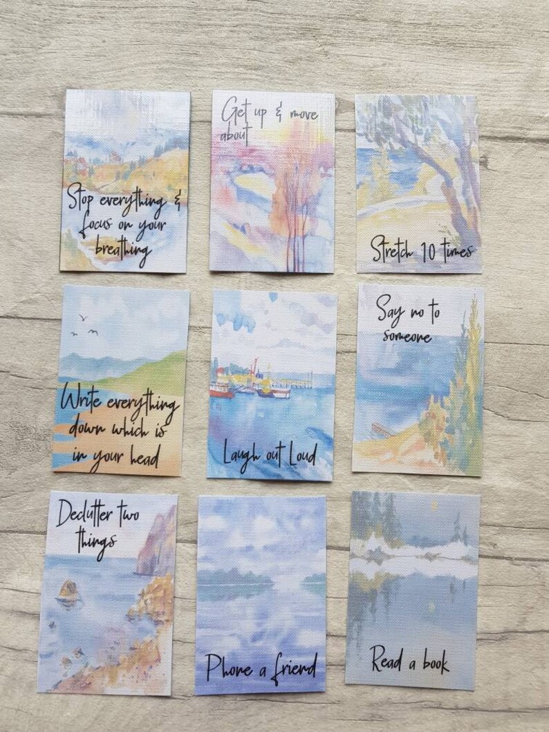 May include: Nine watercolour cards with inspirational quotes and painted landscapes. The quotes include "Stop everything & focus on your breathing", "Get up & move about", "Write everything down which is in your head", "Laugh out loud", "Declutter two things", "Phone a friend", "Stretch 10 times", "Say no to someone", and "Read a book".