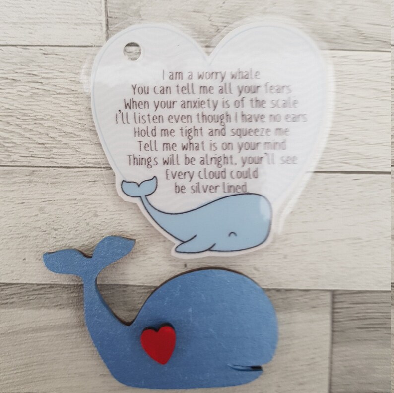 K&ouml;nnte beinhalten: Ein blauer Holzwal mit einem roten Herzen auf seinem Bauch. Ein klares herzf&ouml;rmiges Schild mit einer blauen Walillustration und einem Gedicht &uuml;ber Sorgen ist an den Wal befestigt. Das Gedicht lautet: "Ich bin ein Sorgenwal. Du kannst mir all deine &Auml;ngste erz&auml;hlen. Wenn deine Angst &uuml;bertrieben ist. Ich werde zuh&ouml;ren, obwohl ich keine Ohren habe. Halte mich fest und dr&uuml;cke mich. Sag mir, was dir auf dem Herzen liegt. Alles wird gut, du wirst sehen. Jede Wolke k&ouml;nnte silbern sein."