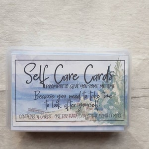 May include: A box of self-care cards with a watercolour design of a lake and a jetty. The text on the box reads "Self Care Cards" and "Prompts to give you some me time. Because you need to take time to look after yourself." The box also states that it contains 36 cards, one for every day of the month and more.