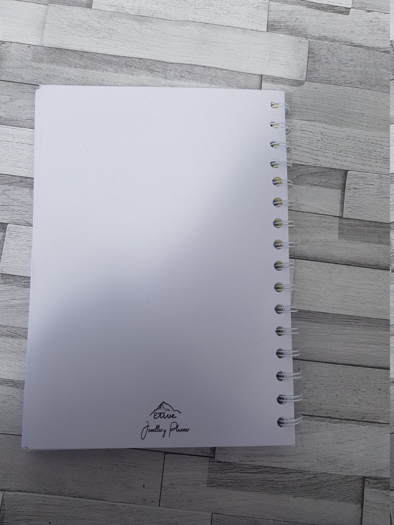 May include: White spiral bound notebook with the text "Etive Jewellery Planner" and a mountain graphic printed on the back cover.