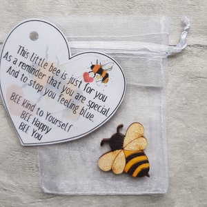 May include: A heart-shaped card with a bee illustration and the text "This little bee is just for you As a reminder that you are special And to stop you feeling blue. BEE Kind to Yourself BEE Happy BEE You"  A small wooden bee with glitter is in a white organza bag.