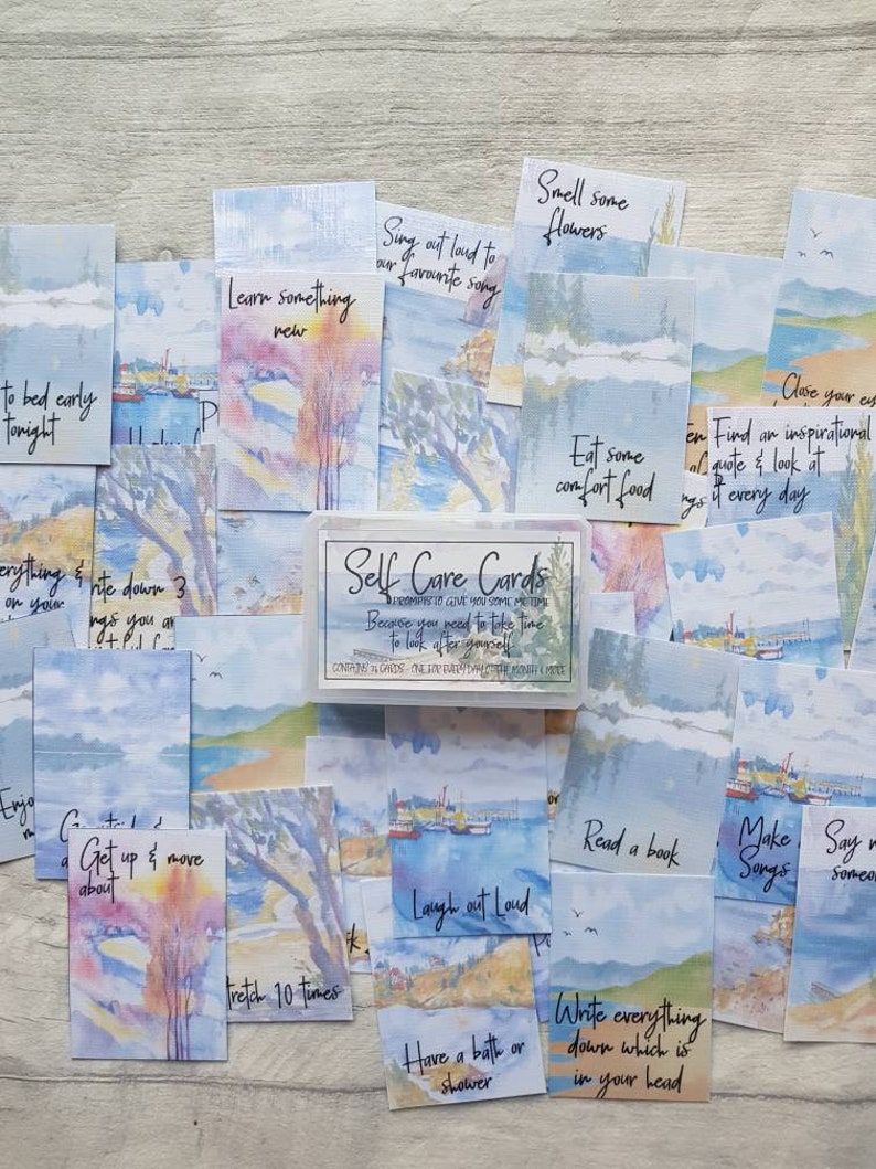May include: A set of watercolour self-care cards with a variety of prompts for self-care, such as "Sing out loud to your favourite song", "Smell some flowers", "Eat some comfort food", "Read a book", "Get up and move about", "Have a bath or shower", "Write everything down which is in your head", "Close your eyes", "Find an inspirational quote and look at it every day", "Make songs", "Say something nice to someone", "Laugh out loud", "Stretch 10 times", "Learn something new", "Go to bed early tonight", "Do anything & write down 3 things you are grateful for".