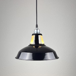 Könnte beinhalten: Eine schwarze Pendelleuchte mit glänzender Oberfläche. Die Leuchte hat einen runden Schirm und ein schwarzes Kabel. Die Leuchte ist von der Decke abgehängt. Die Leuchte ist ein modernes Design.
