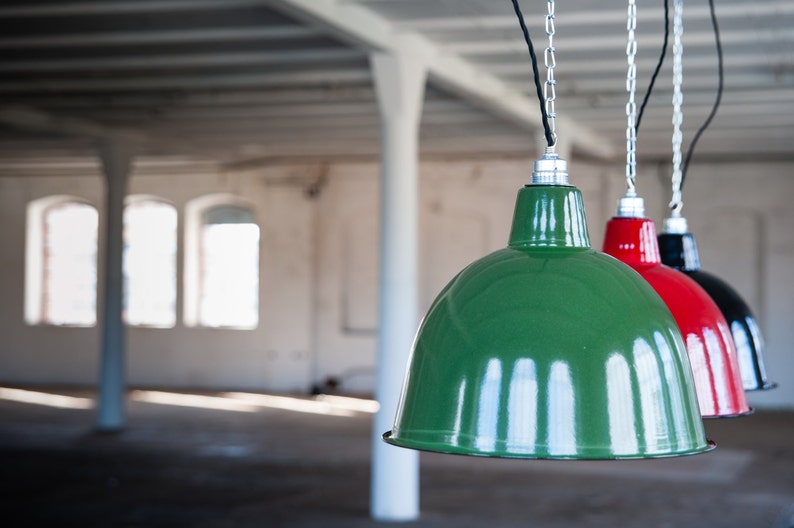 May include: Three industrial pendant lights hanging from the ceiling. The lights are made of metal and have a green, red, and black finish.