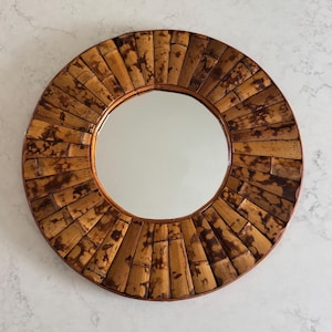 May include: A round wall mirror featuring a frame constructed from numerous small, vertically arranged segments of mottled brown and tan bamboo. The reflective glass center is circular, surrounded by the textured, natural wood-toned bamboo pieces.