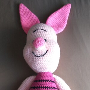May include: A pink crocheted pig stuffed animal with black stripes on its body. The pig has a pink nose and a smiling face.