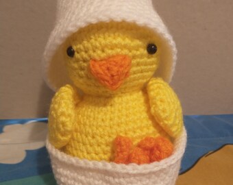 May include: A crocheted yellow chick wearing a white crocheted hat and sitting inside a white crocheted egg.