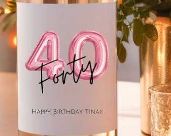 May include: A white wine bottle with a pink and white label. The label has a pink number 40 with the word "Forty" written in black script. The label also says "Happy Birthday Tina!"