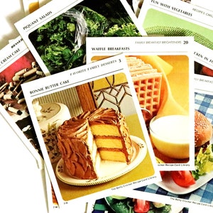 May include: A selection of vintage recipe cards from the Betty Crocker Recipe Card Library. The cards display images of various dishes, including a layered cake with chocolate icing, waffles, and a burger. Other cards show salads and vegetables.