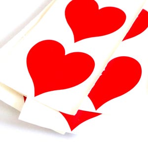 May include: Close-up of several white cards with large, bright red heart shapes. The hearts are evenly spaced and appear to be stickers or decals. The image is well-lit, highlighting the vibrant red against the white background.
