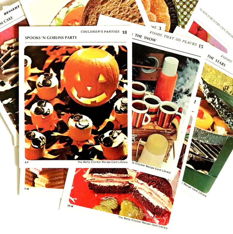 May include: A selection of vintage recipe cards from The Betty Crocker Recipe Card Library. One card shows a carved pumpkin and cupcakes for a "Spooks 'N Goblins Party." Other cards display various foods and recipes.