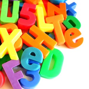 May include: A collection of plastic alphabet letters and numbers in various bright colors including red, orange, yellow, green, blue, and purple. The pieces are scattered in a pile, featuring both uppercase and lowercase characters in a bold font.