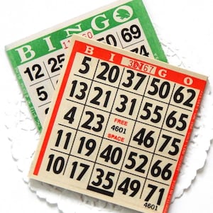 May include: Two square paper bingo cards with black numbers on a cream background. The top card has a green border with the word BINGO in green letters. The bottom card has a red border with the word BINGO in red letters and a central free space.