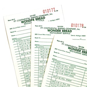 May include: Three vintage Wonder Bread Restaurant Service order forms. The forms are white with black text, including the company name, address, and a list of items with codes and weights. The forms are slightly angled.
