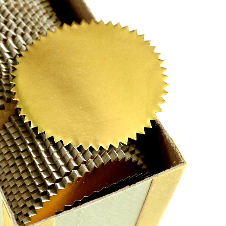 May include: A stack of circular gold foil seals with serrated, starburst-style edges. The seals are arranged in a vertical column, showing the metallic finish and the jagged, die-cut perimeter of each individual adhesive label in the collection.