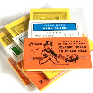 May include: A stack of Monopoly game cards, including a Chance card with a cartoon of Mr. Monopoly riding a horse, a Title Deed card for Park Place, and a yellow card with the text "Take a Walk on the Board Walk Advance Token to Board Walk".