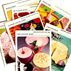 May include: A selection of vintage recipe cards from the Betty Crocker Recipe Card Library. The cards showcase colourful illustrations of dishes like soda fountain shakes, banana bobs, and cranberry pancake supper. The cards are labelled with recipe names and page numbers.