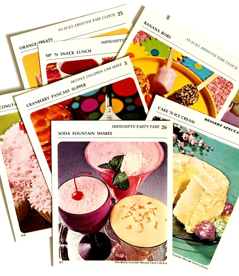 May include: A selection of vintage recipe cards from the Betty Crocker Recipe Card Library. The cards showcase colourful illustrations of dishes like soda fountain shakes, banana bobs, and cranberry pancake supper. The cards are labelled with recipe names and page numbers.