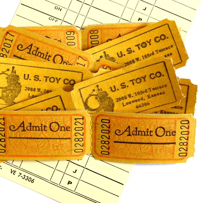 May include: A collection of yellow paper admission tickets with black text reading Admit One and U.S. Toy Co. 2008 W. 103rd Terrace Leawood, Kansas 66206. The tickets feature unique serial numbers and a small circular graphic, layered over a white grid sheet.