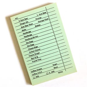May include: A retro green order pad featuring a list of classic diner menu items such as burgers, hot dogs, and shakes. The pad has a grid for writing and options for coffee and milk. The word "TOTAL" is printed at the bottom.
