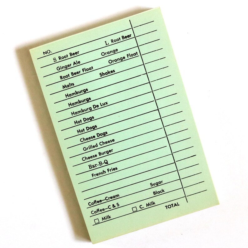 May include: A retro green order pad featuring a list of classic diner menu items such as burgers, hot dogs, and shakes. The pad has a grid for writing and options for coffee and milk. The word "TOTAL" is printed at the bottom.