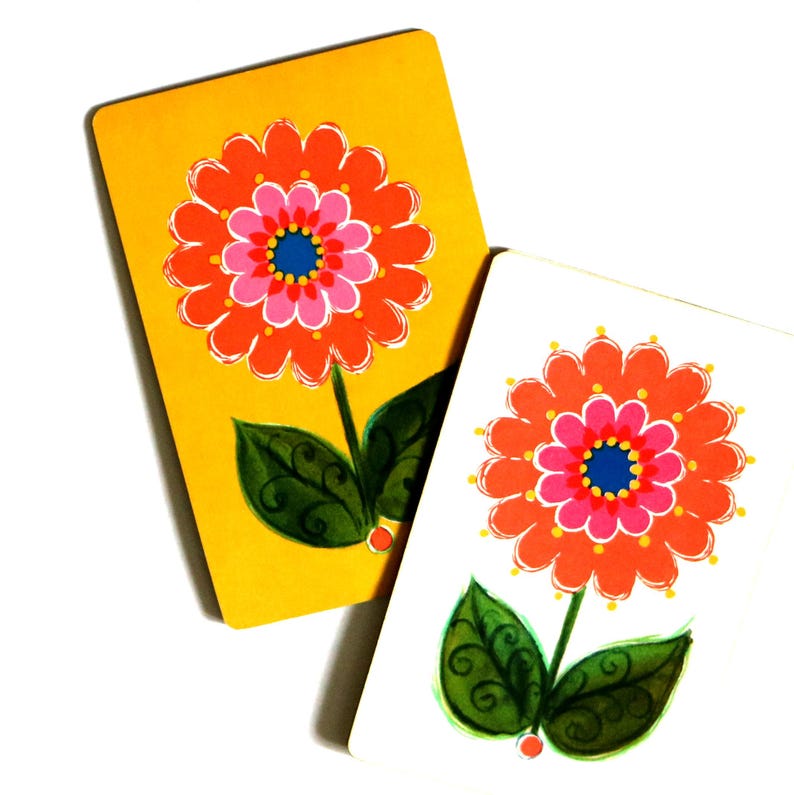 May include: Two rectangular cards featuring a floral illustration. One card has a yellow background, the other a white background. Both display an orange and pink flower with a blue center, a green stem, and two green leaves with dark swirls.
