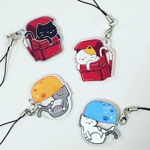 May include: Four colorful cat charms with different colored backgrounds. Each charm features a white cat with a different colored hat or backpack. The charms are attached to a black string.