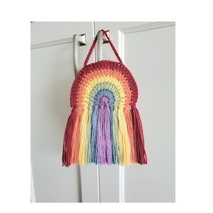 May include: A rainbow-colored crocheted wall hanging with tassels. The hanging is shaped like an arch and is made with different shades of yarn.