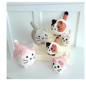 Puede incluir: Cinco juguetes de crochet con forma de gato en varios colores y patrones. Los gatos están todos sentados o de pie en un estante blanco.