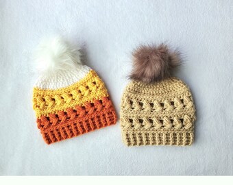 May include: Two crocheted hats with faux fur pom poms. One hat is white, yellow, and orange, and the other is beige.