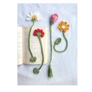 May include: Four crocheted flower bookmarks in different colors, including white, pink, red, and yellow. The bookmarks are attached to a book.