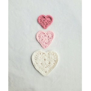 May include: Three crocheted hearts in a gradient of pink and white. The largest heart is white, the middle heart is light pink, and the smallest heart is a darker pink.