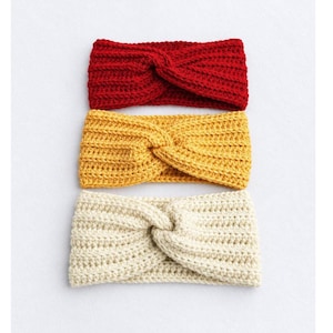 May include: Three crocheted headbands stacked vertically, each featuring a central twist detail and a ribbed texture. The top headband is bright red, the middle one is mustard yellow, and the bottom headband is a soft cream color.