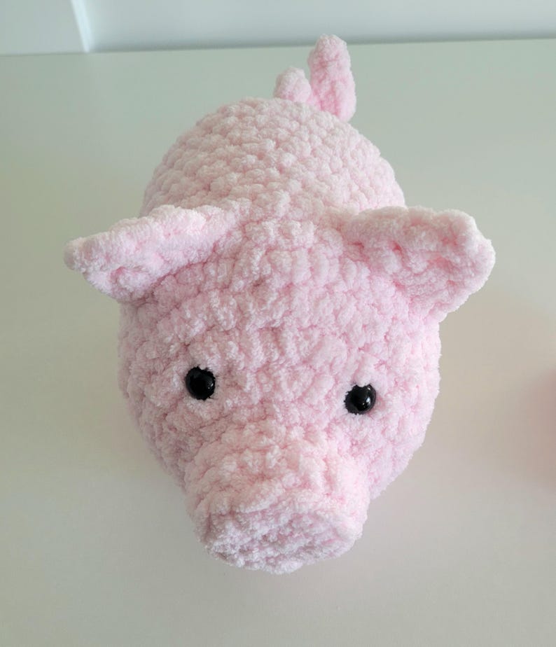 May include: A handmade, plush pink pig with black eyes and floppy ears. The pig is made of a soft, textured material and has a small tail. The pig is a cute, cuddly toy.