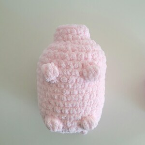 May include: A handmade, light pink, plush toy shaped like a penguin. The penguin has small, rounded arms and feet, and a textured, fluffy surface. The toy is made of soft, chunky yarn.