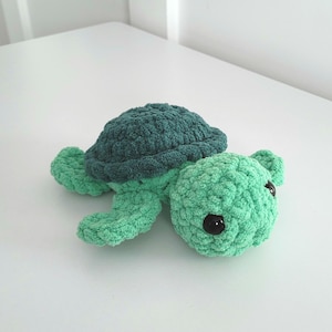 Puede incluir: Un juguete de peluche de tortuga verde y azul verdoso tejido a crochet con ojos negros.