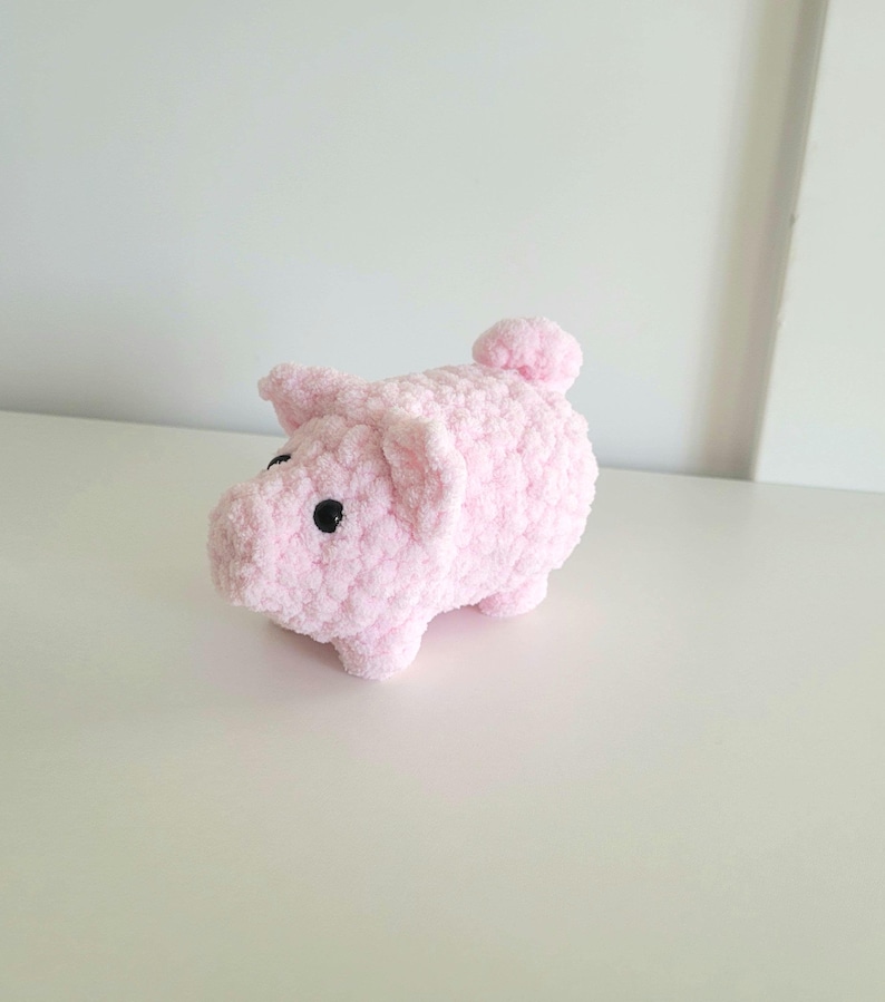 May include: A handmade pink crocheted pig with black eyes and a small tail. The pig is made of soft, fluffy yarn and has a rounded body and small legs. This adorable stuffed animal is a cute gift for kids or a charming home decor item.