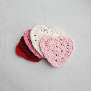 May include: Four crocheted heart-shaped coasters in shades of red, pink, and white. The coasters are stacked on top of each other.