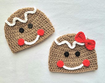 May include: Two crocheted gingerbread person hats. One hat has a red bow and the other has a black button. Both hats have white icing and red cheeks.