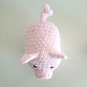 May include: A handmade, light pink crocheted pig with small black eyes, floppy ears, and a curly tail. The plush toy is made of soft, textured yarn, and is a whimsical, cuddly creation.
