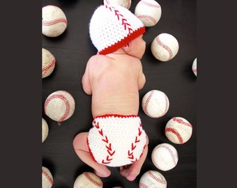 May include: A baby wearing a white crocheted baseball cap with red stitching and a white crocheted diaper with red stitching, surrounded by baseballs.