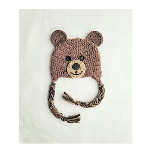 May include: Brown crocheted bear hat with long brown and tan braids. The hat has black button eyes and a brown nose.