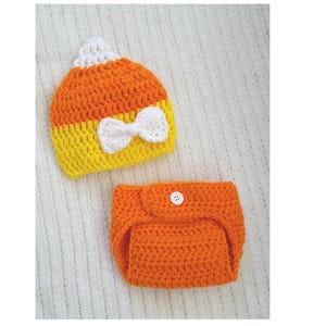 May include: A crocheted candy corn hat and diaper cover set for a baby. The hat is orange, yellow, and white with a white bow. The diaper cover is orange.