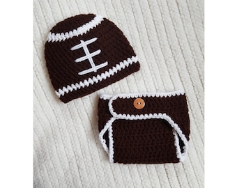 May include: A dark brown crochet hat and diaper cover set designed to resemble an American football. The hat features white horizontal stripes and white laces. The diaper cover has white trim and a single round brown button at the center front.