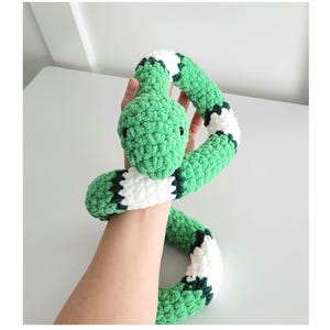 May include: A green and white crocheted snake toy. The snake is curled up in a circle and has a black eye.