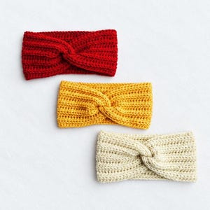 Puede incluir: Tres diademas de ganchillo con un diseño frontal retorcido. Las diademas se presentan en colores sólidos: un rojo vibrante, un amarillo mostaza y un crema, cada una mostrando una textura acanalada consistente en todo el tejido.