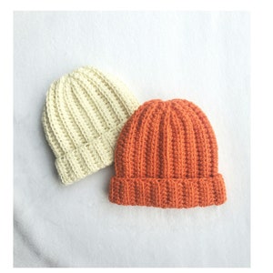 May include: Two crocheted hats, one in a cream color and the other in a bright orange color. Both hats have a ribbed texture.