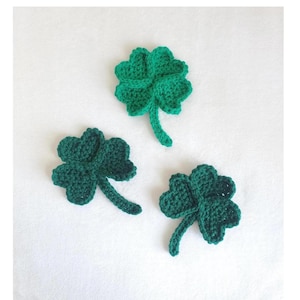 Puede incluir: Tres tréboles de cuatro hojas de ganchillo verde sobre un fondo blanco.